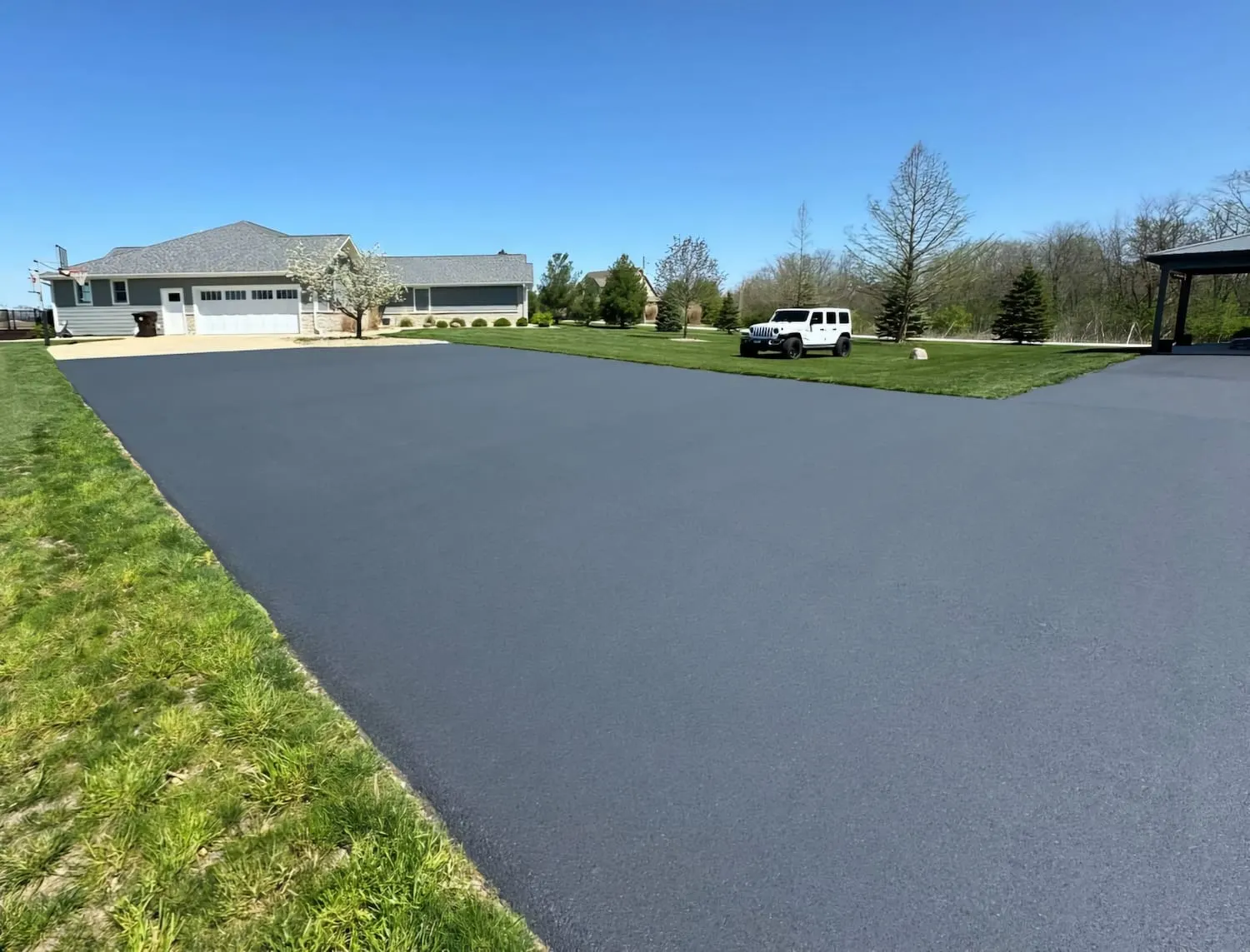 Freshly paved asphalt driveway extending across a green lawn in front of a suburban home